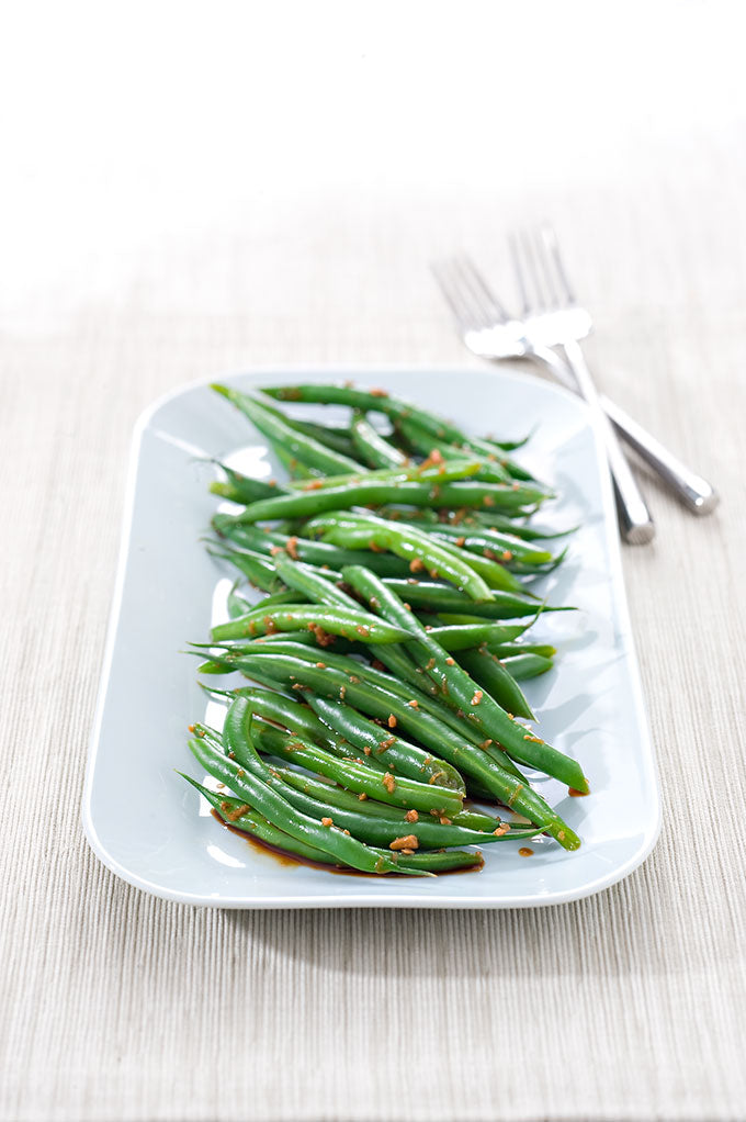 A platter of green beans garnished with sesame seeds, drizzled with soy sauce and ginger.
