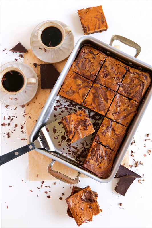 A tray of pumpkin swirl brownies with chocolate shavings and two cups of coffee