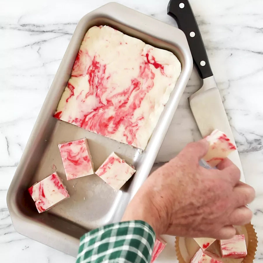 A hand cutting marbled dessert in a stainless steel jelly roll pan.