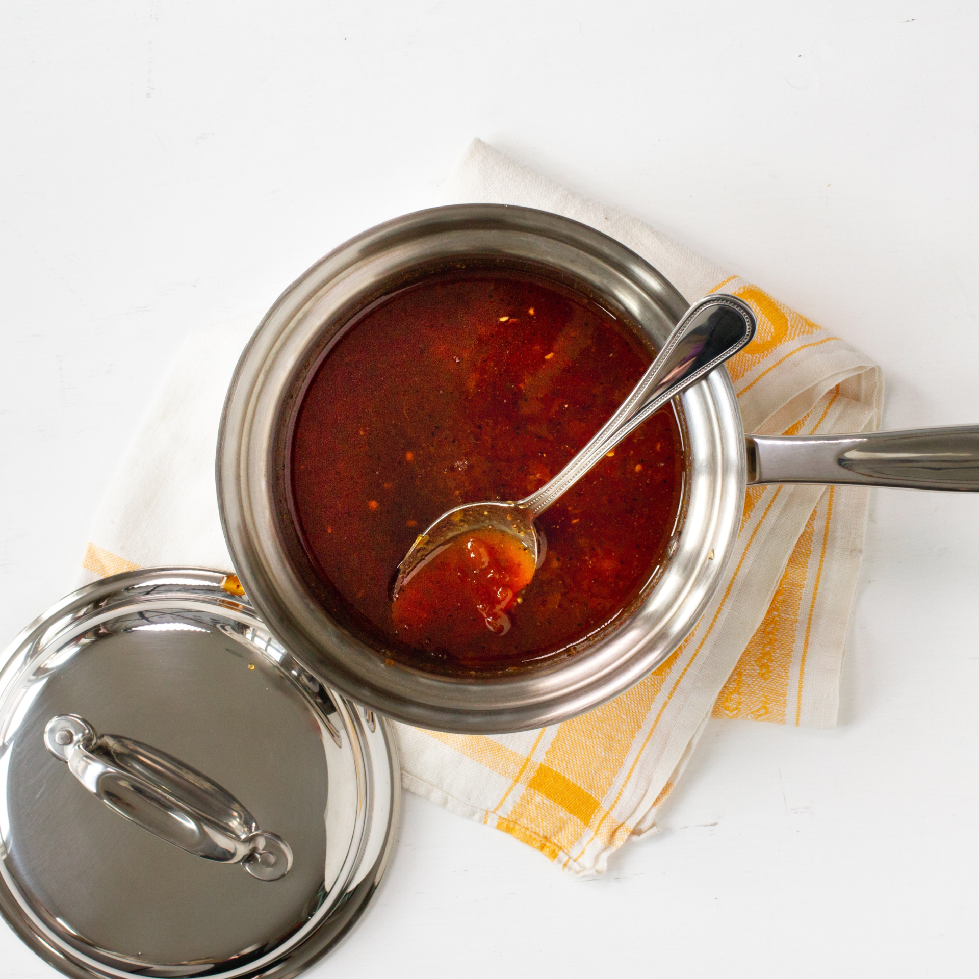 A stainless steel saucepan with sauce and a spoon, placed on a towel.