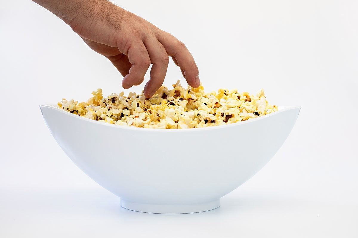 A hand reaching into a white salad bowl filled with popcorn