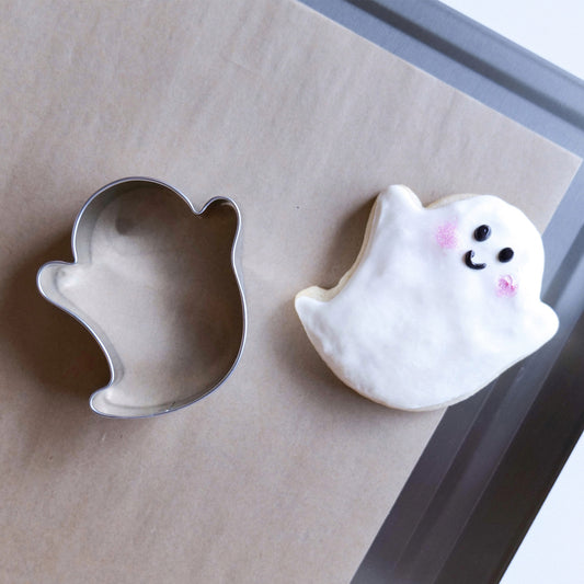 3.35" ghost-shaped cookie cutter next to a decorated ghost cookie with a smiley face.