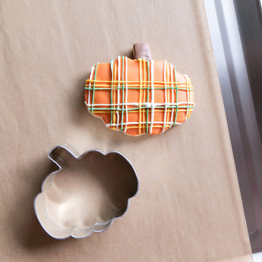 A 3-inch pumpkin-shaped cookie cutter next to a decorated pumpkin cookie.
