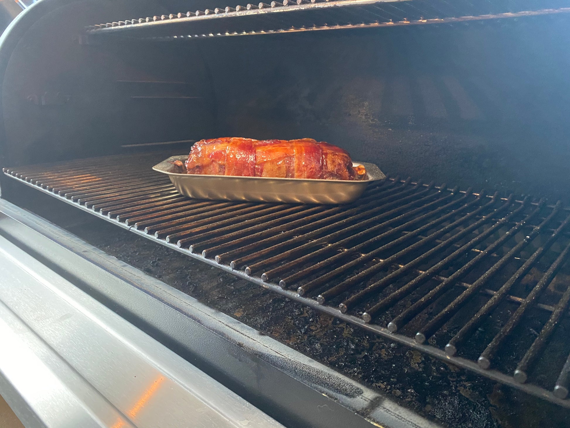A stainless steel mini jelly roll pan with meatloaf inside, placed in an oven.