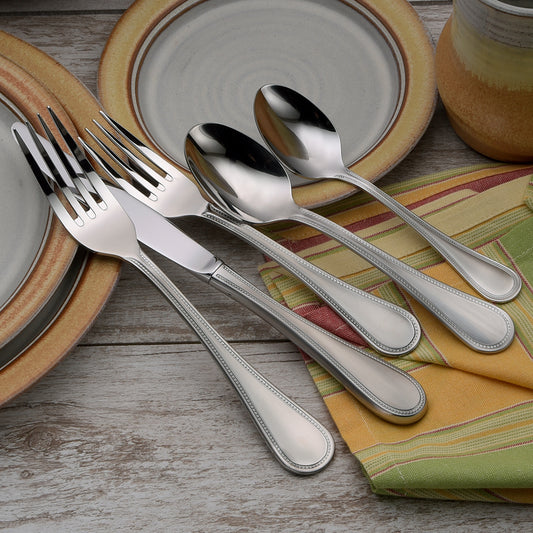 Set of stainless steel utensils including forks and spoons on a table with plates and a cloth.