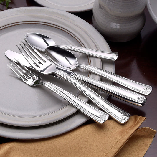 Four pieces of Prestige flatware including a knife, fork, and spoon on a plate with a napkin.
