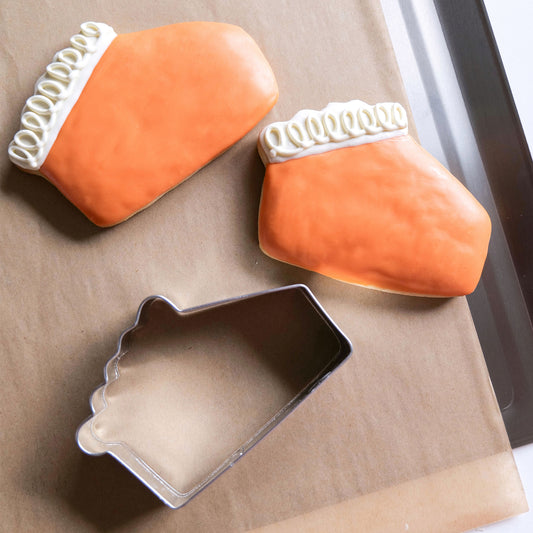 Two decorated pie slice cookies and a pie slice cookie cutter on parchment paper