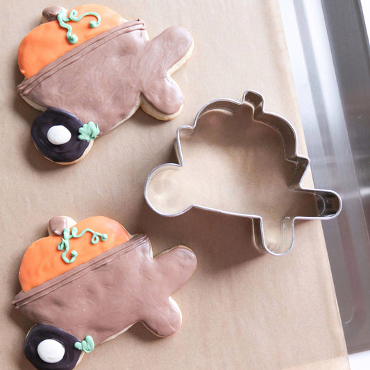 Two decorated pumpkin cookies and a 4-inch pumpkin cookie cutter on parchment paper.