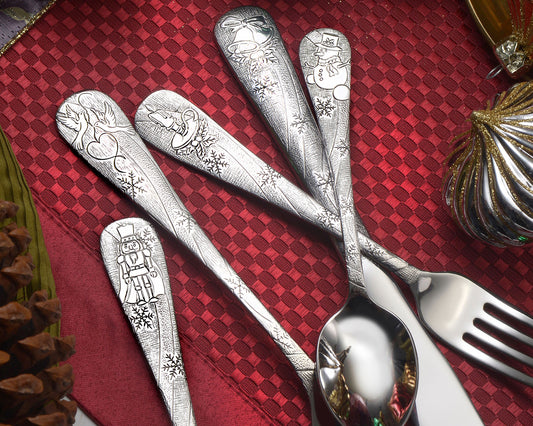 Four pieces of engraved holiday flatware on a red tablecloth, featuring festive designs.