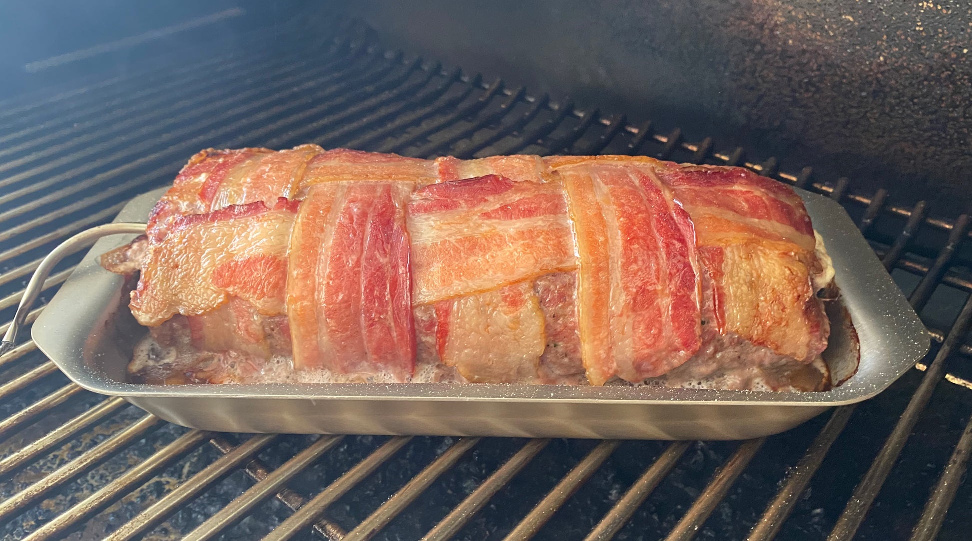 Bacon-wrapped meatloaf in a mini jelly roll pan on a grill