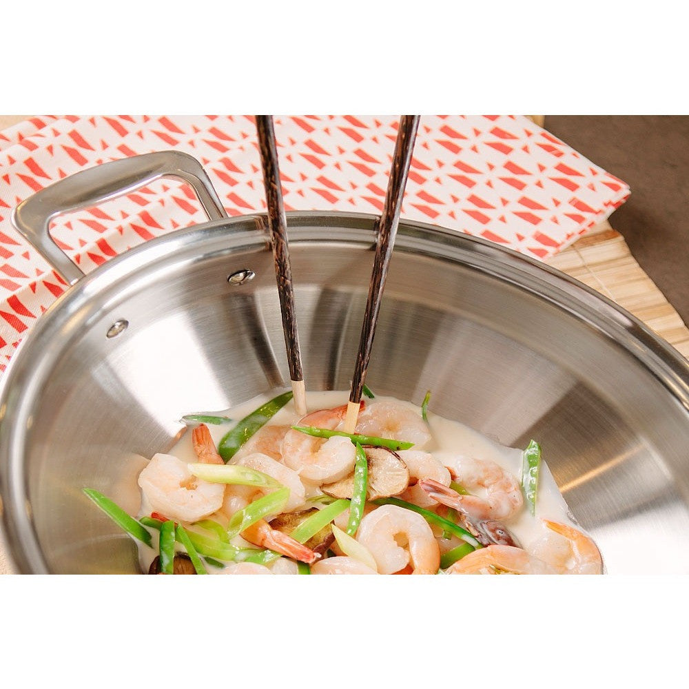 Close-up of shrimp and vegetables being cooked in a stainless steel wok with chopsticks