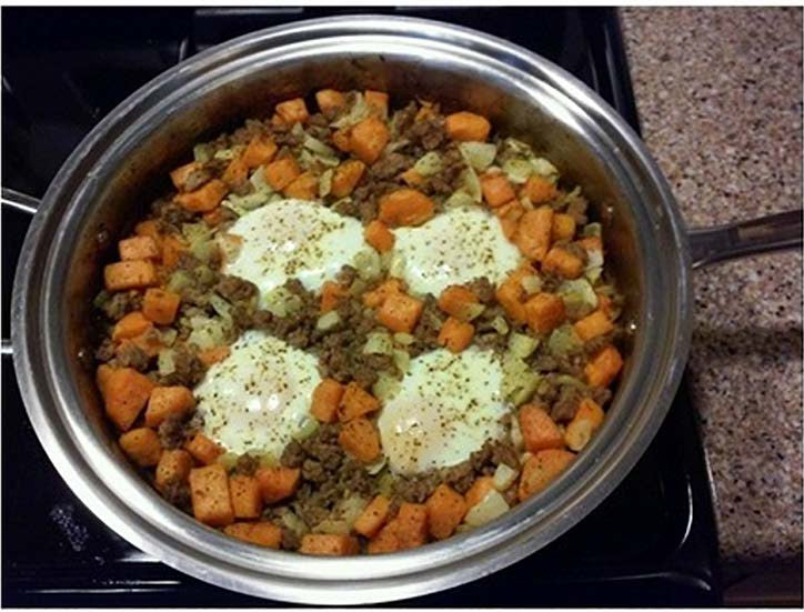 Sweet potato hash with turkey sausage and four baked eggs in a stainless steel sauté pan on stovetop