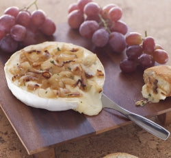 Baked Brie topped with caramelized onions, served with grapes and bread on a wooden board