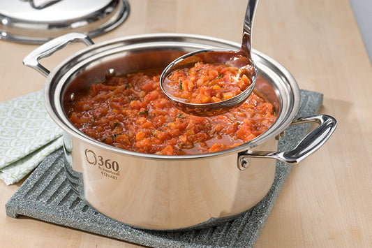 Angled view of 360 Cookware stainless steel stockpot filled with marinara sauce, ladle resting inside on a wooden countertop