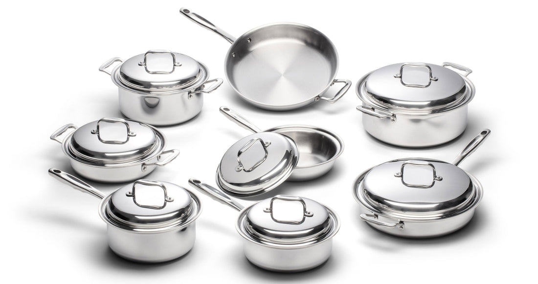 Angled overhead view of eight stainless steel cookware pieces showing pots and pans with lids and handles on white background