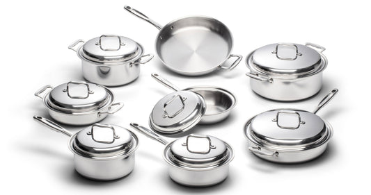 Angled overhead view of eight stainless steel cookware pieces showing pots and pans with lids and handles on white background
