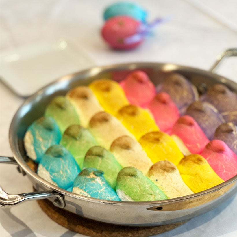 Close-up of Peeps s'mores dessert casserole in a stainless steel skillet showcasing rows of colorful Peeps browned on top over a graham cracker crust