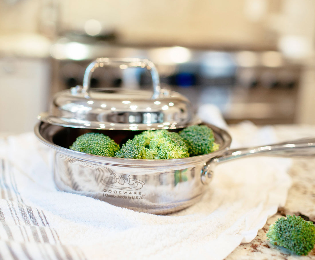 Close-up of stainless steel saucepan with lid slightly ajar showcasing broccoli and polished reflective finish with blurred kitchen background