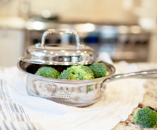 Close-up of stainless steel saucepan with lid slightly ajar showcasing broccoli and polished reflective finish with blurred kitchen background