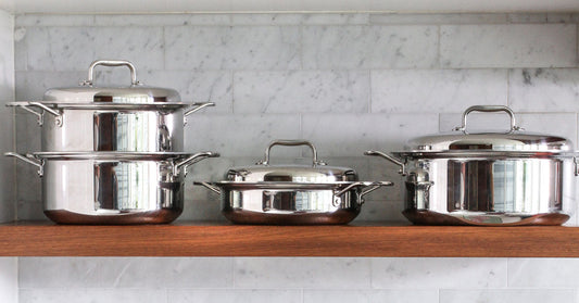 Three pieces of stainless steel 360 Cookware on a wooden shelf, showcasing their design and quality.