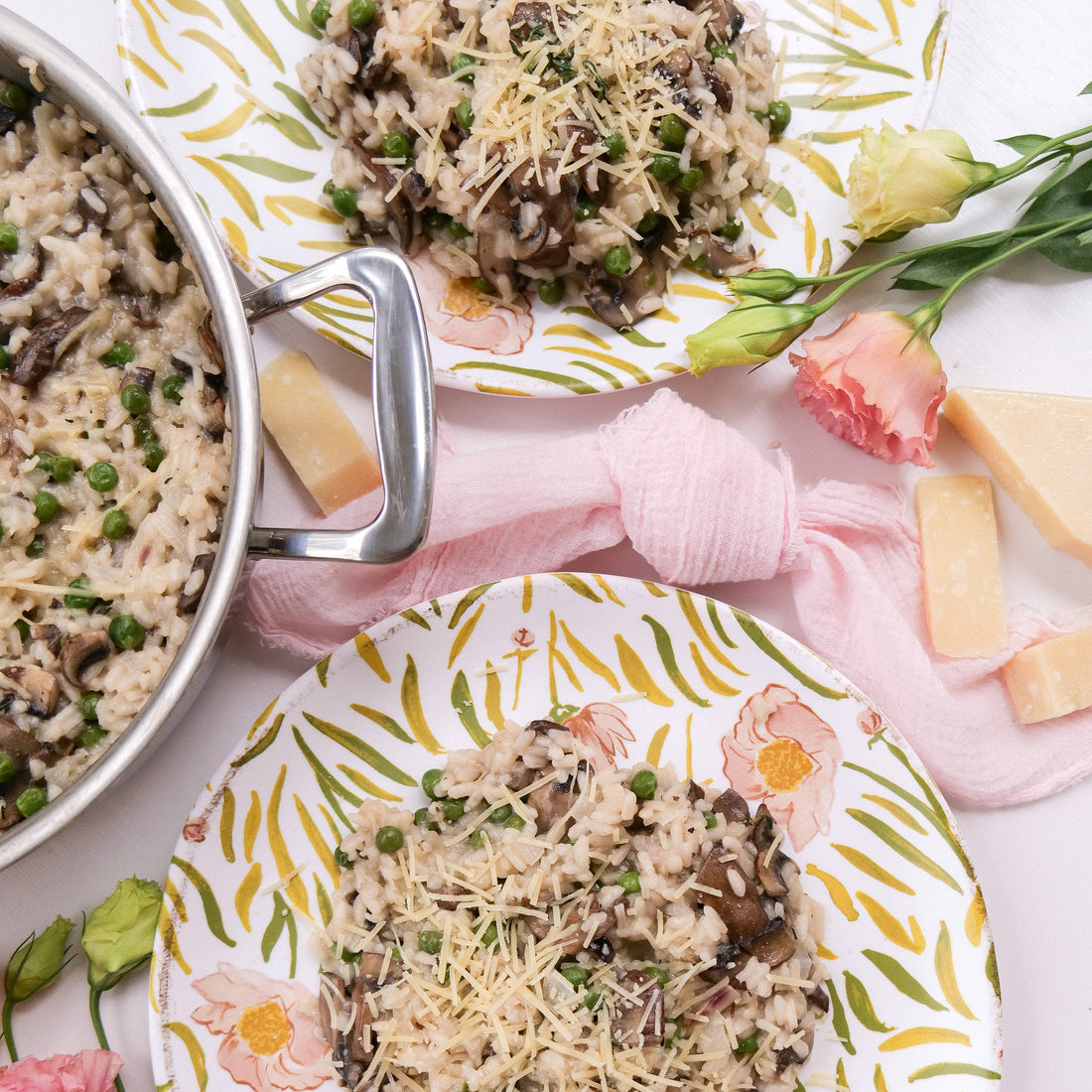 Mushroom and pea risotto served on patterned floral plates with grated Parmesan, a stainless pan handle, and a pink cloth napkin
