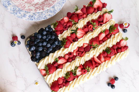 Overhead view of 4th of July sugar cookie flag fruit pizza with piped cream stripes and red, white, and blue berries on marble