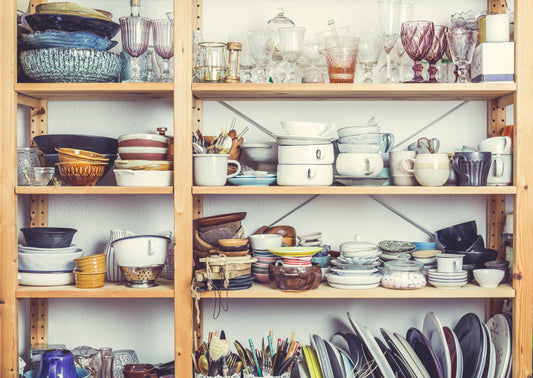 A cluttered kitchen shelf filled with various dishes, glasses, and utensils.