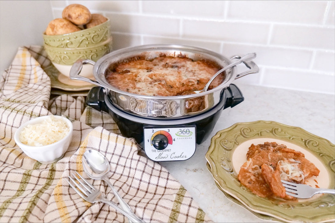 Slow cooker with bubbling cheesy tomato casserole on a kitchen countertop with bowls of shredded cheese and potatoes