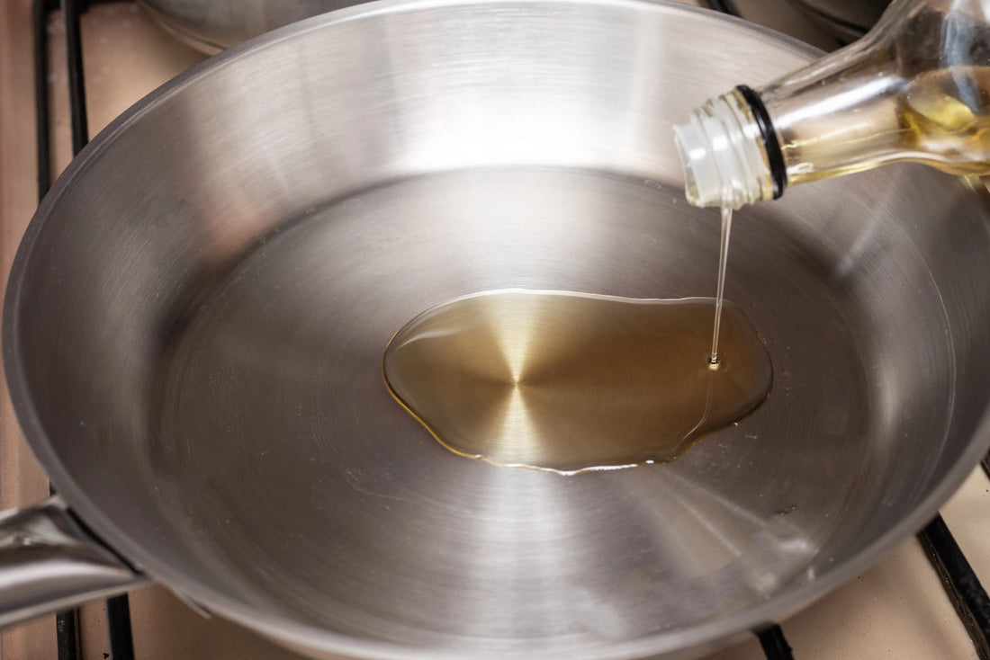 Bottle pouring oil into a stainless steel frying pan on a stovetop