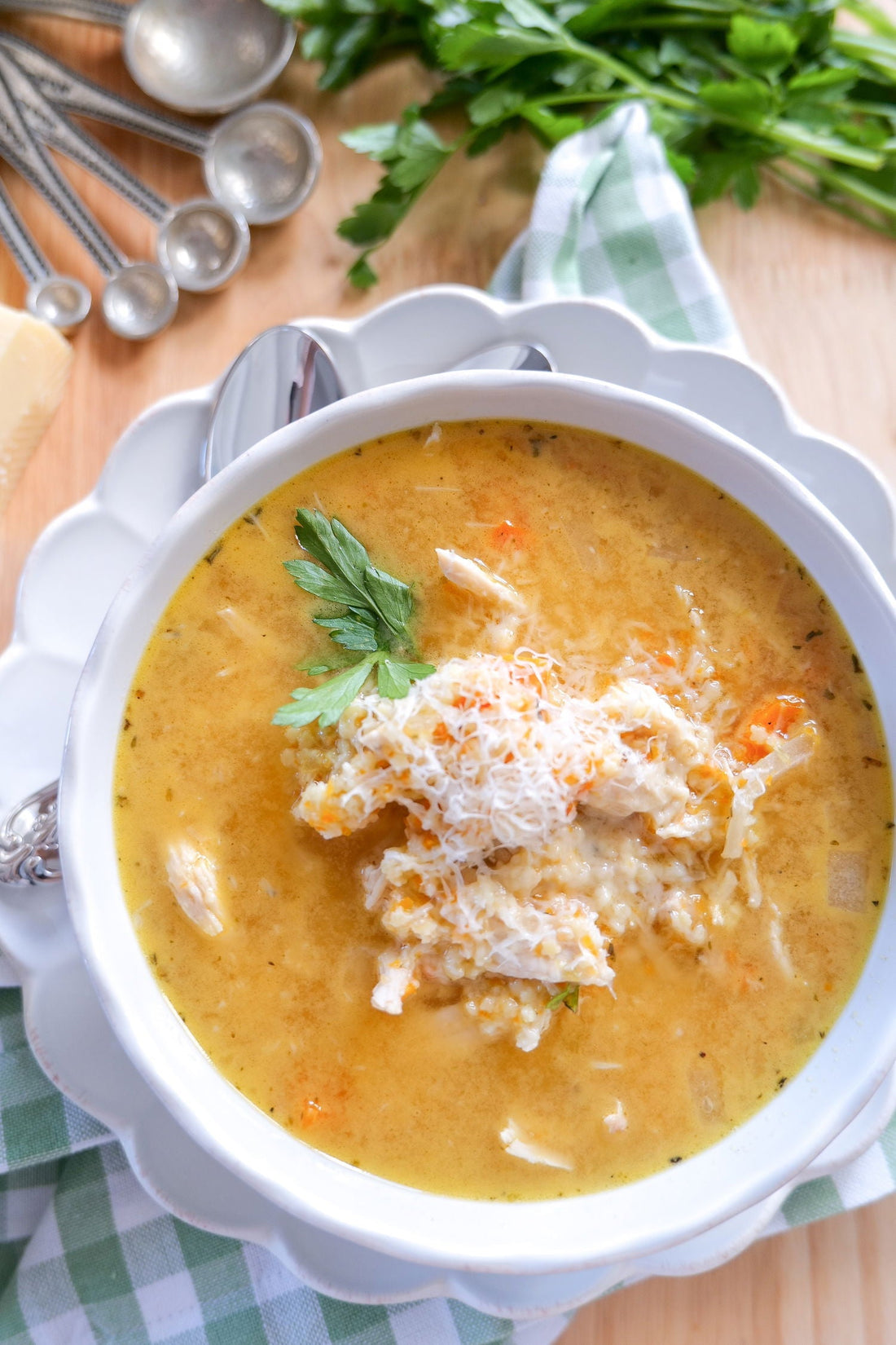 Bowl of Italian Penicillin soup topped with shredded Parmesan and parsley on a white scalloped plate over a green checkered napkin