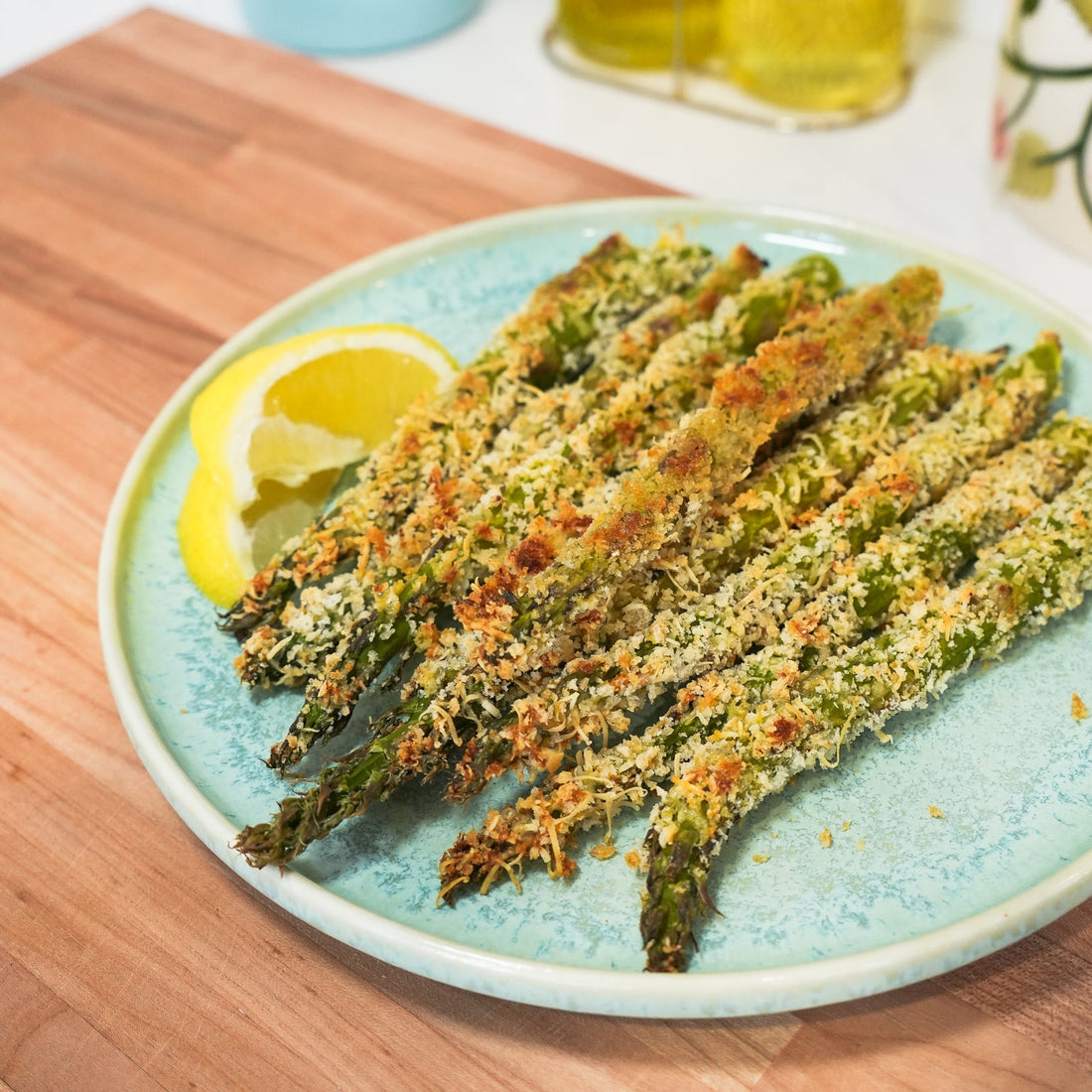 Top-down view of panko and Parmesan crusted asparagus spears showcasing golden toasted breadcrumb crust on a blue plate with a lemon wedge