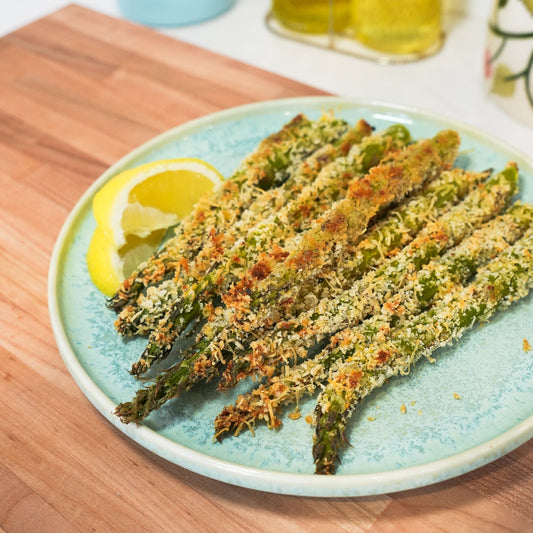 Top-down view of panko and Parmesan crusted asparagus spears showcasing golden toasted breadcrumb crust on a blue plate with a lemon wedge