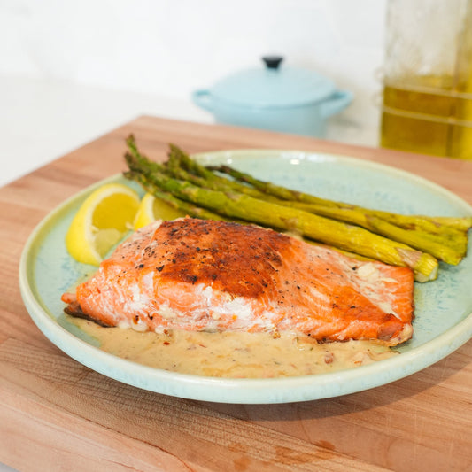 Pan-seared salmon fillet with lemon cream sauce, roasted asparagus, and lemon wedges on a blue plate