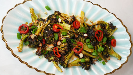 Roasted broccoli tossed with sliced red chiles, scallions, and almond slivers on a scalloped white and blue-rimmed plate
