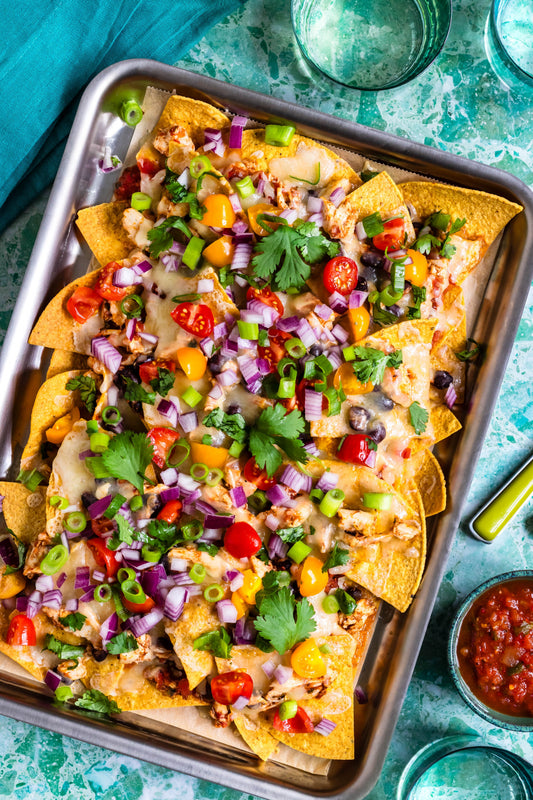 Sheet-pan nachos with melted cheese, black beans, cherry tomatoes, diced red onion and cilantro on a metal baking sheet