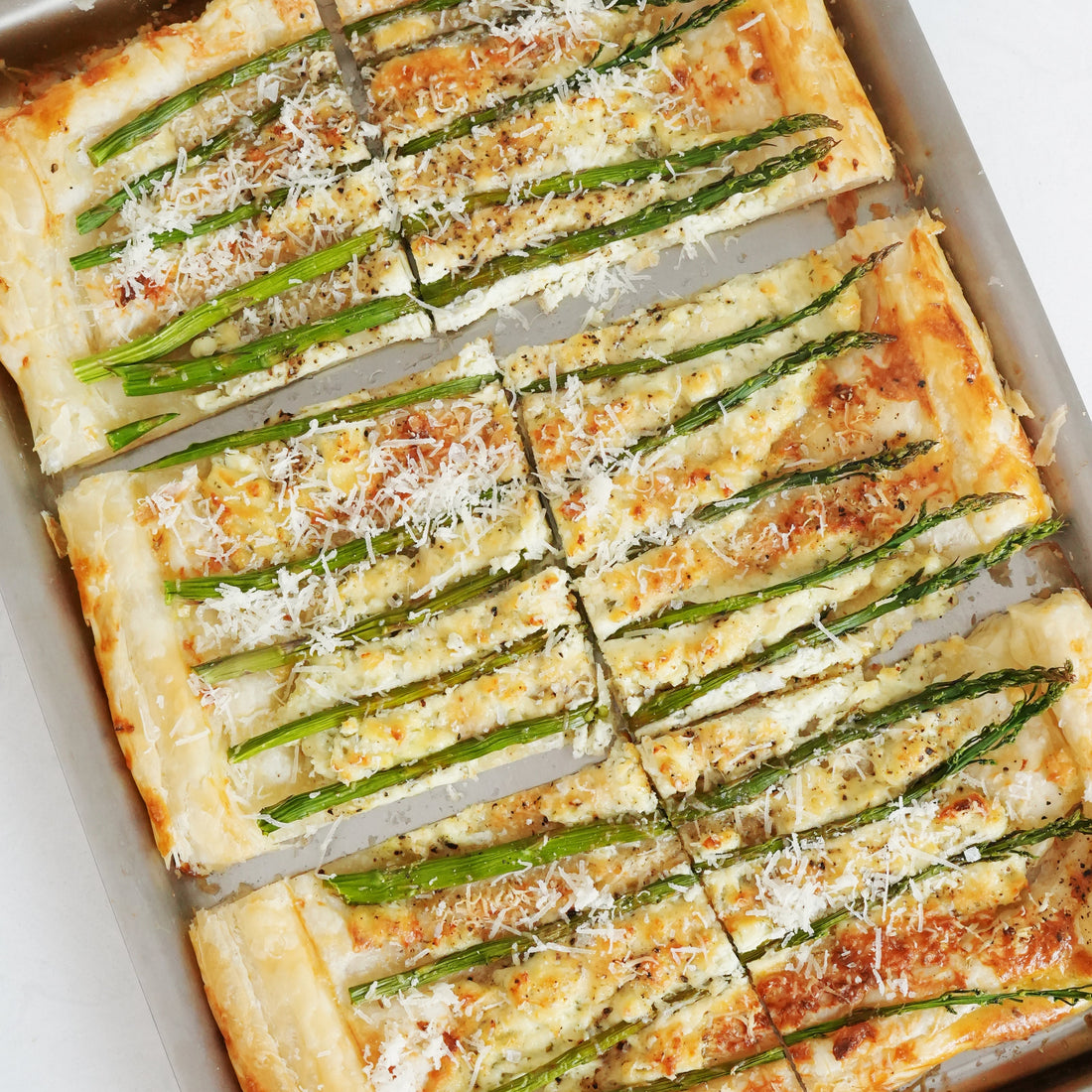 Top down view of asparagus tart showing sliced puff pastry topped with asparagus spears and grated cheese on a baking sheet