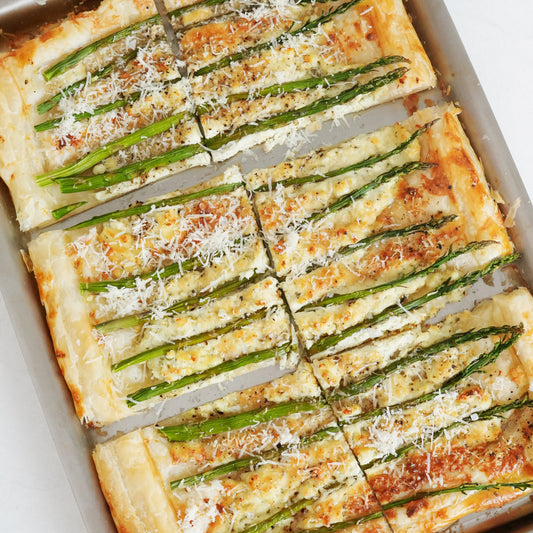 Top down view of asparagus tart showing sliced puff pastry topped with asparagus spears and grated cheese on a baking sheet