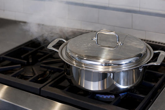 view of stainless steel covered sauté pan showing tight-fitting lid and side handles on a gas stove with steam rising