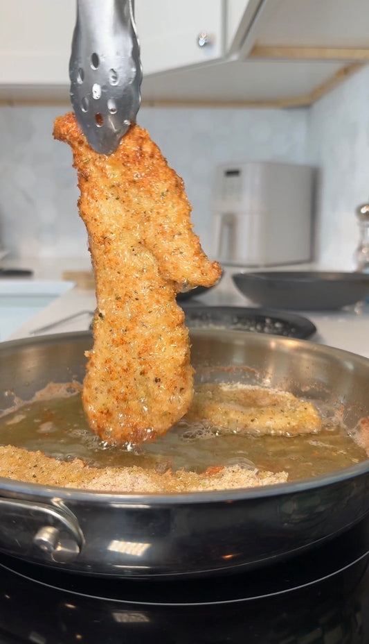 Breaded chicken cutlet frying in a skillet, lifted with metal tongs in a home kitchen