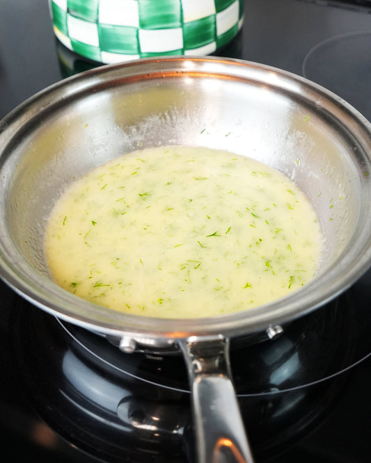 Lemon butter sauce resting in a stainless-steel pan on a black stovetop, flecked with lemon zest