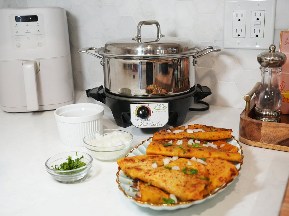 Birria-style tacos on a plate with diced onion and cilantro in the foreground, stainless-steel slow cooker on the kitchen counter behind them