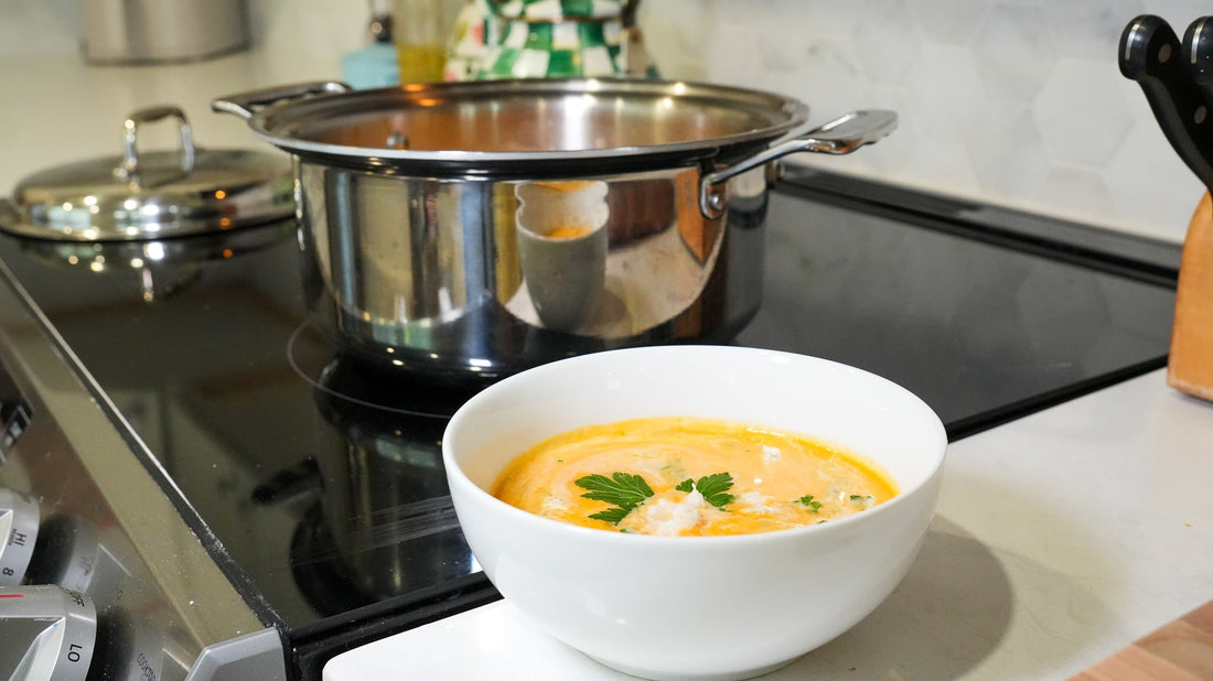 Bowl of crab bisque garnished with parsley on a stovetop with a stainless pot simmering in the background