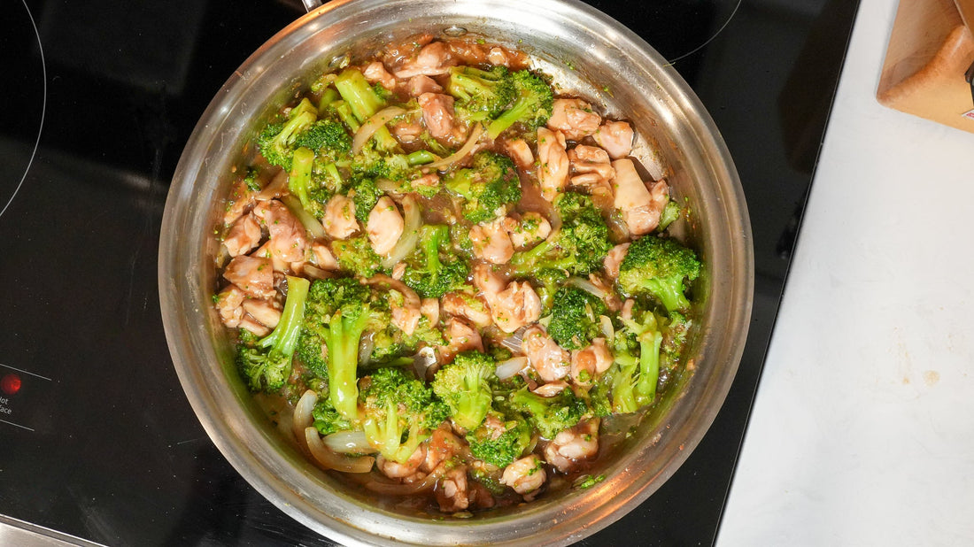 Overhead view of chicken and broccoli stir fry cooking in a stainless steel pan on a black stovetop