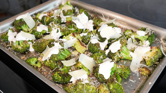 Roasted broccoli on a stainless steel baking sheet topped with dollops of Greek yogurt Caesar dressing and shaved Parmesan