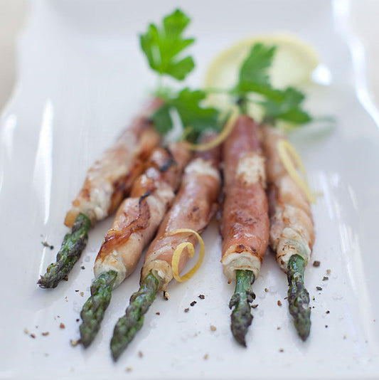 Five prosciutto-wrapped asparagus spears garnished with parsley and lemon slices
