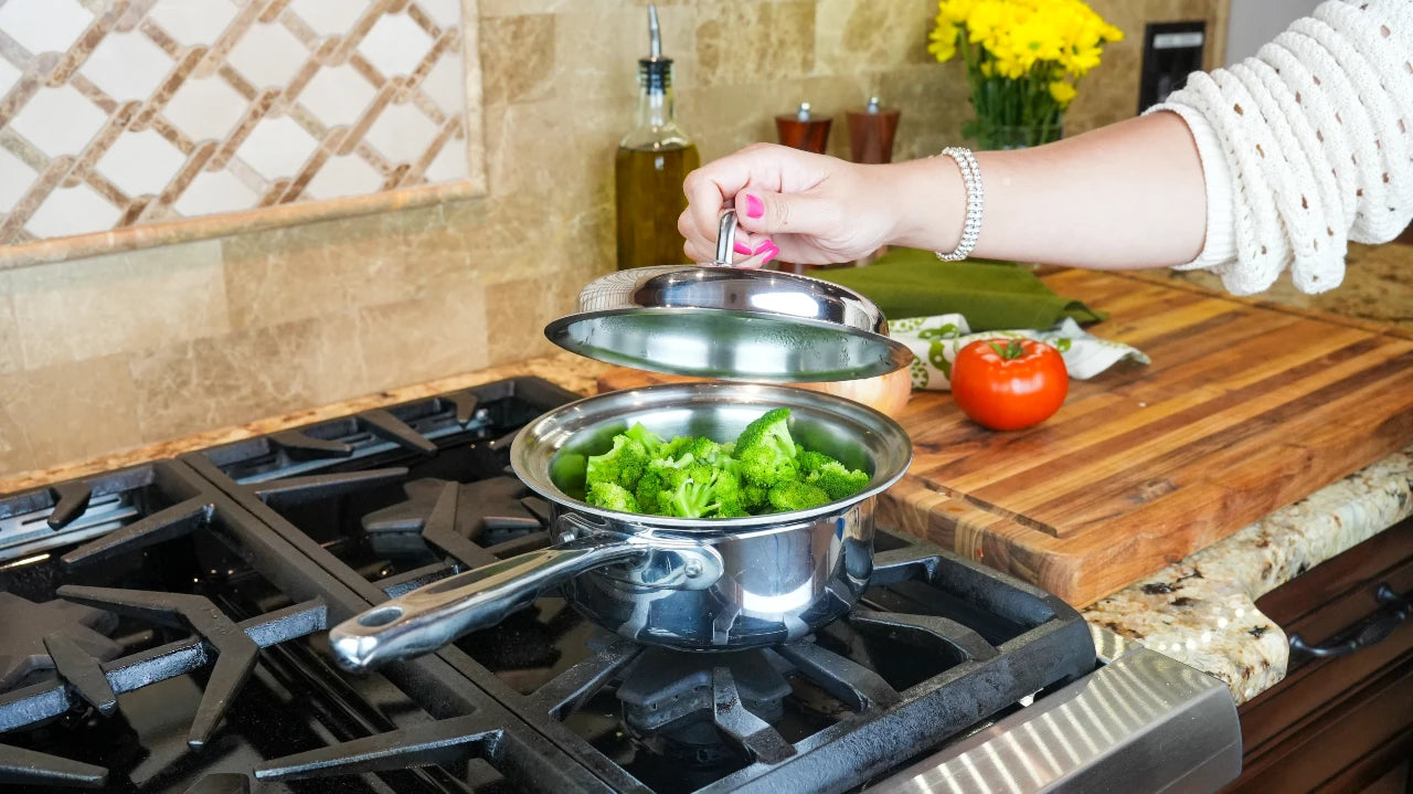 Person preparing food on a stove with pots and a tomato on a wooden cutting board.