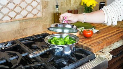Person preparing food on a stove with pots and a tomato on a wooden cutting board.