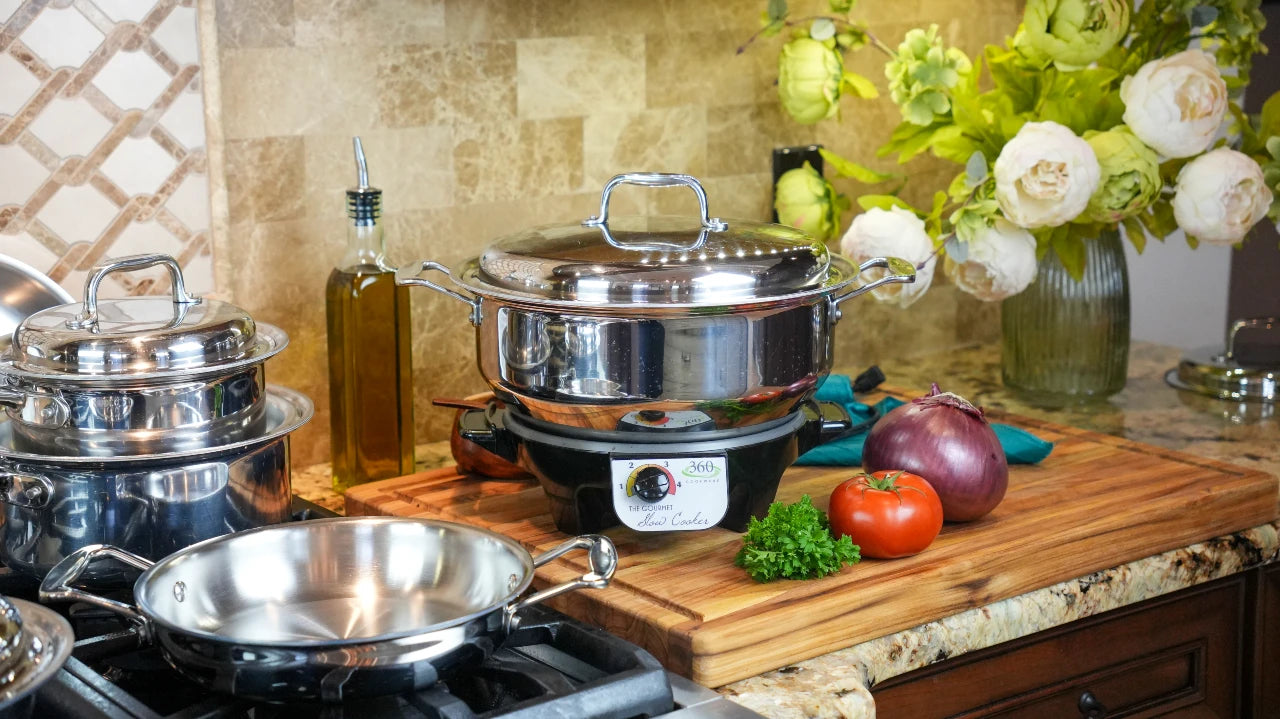 Stainless steel cookware set on a kitchen counter with a cutting board and vegetables.
