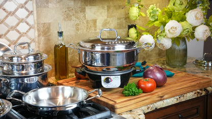 Stainless steel cookware set on a kitchen counter with a cutting board and vegetables.