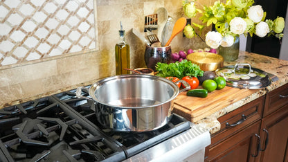 Kitchen counter with cooking pot, vegetables, and utensils on a stove.